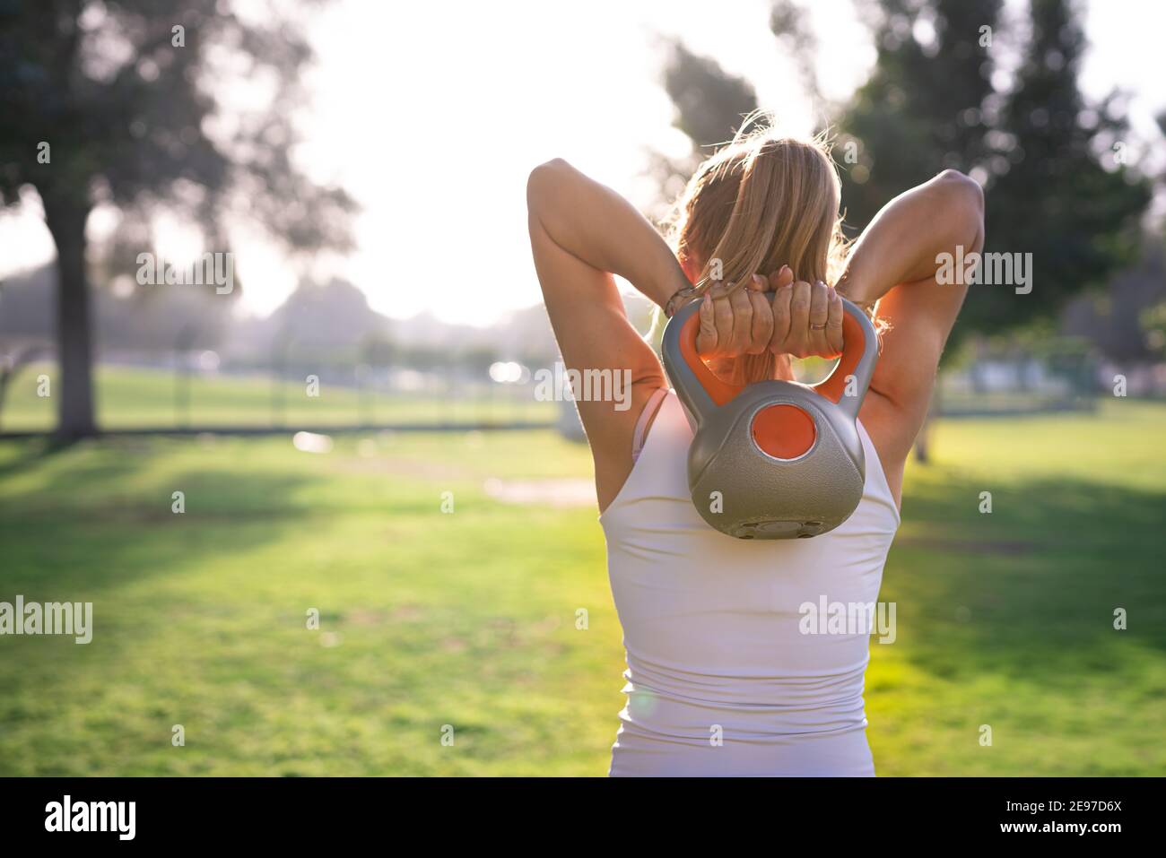 Eine junge Frau nimmt im Grünen des Parks Übungen an, die in rosa Yogahosen gekleidet und auf einer Yogamatte positioniert sind. Stockfoto