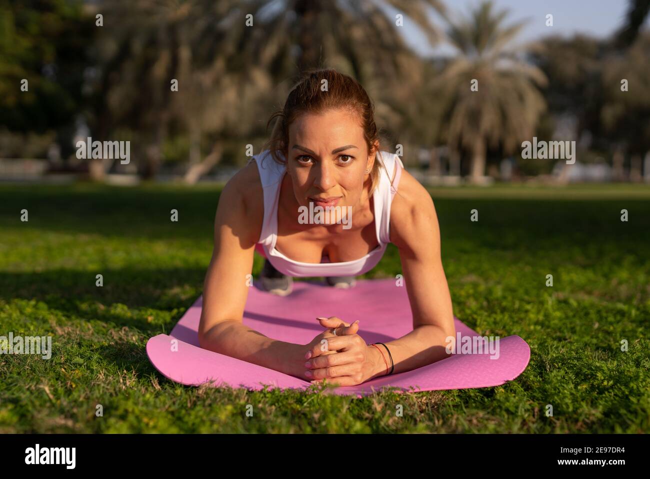 Im ruhigen Ambiente der Natur widmet sich eine junge Dame der Kunst des Yoga, die in leuchtend rosa Yoga-Kleidung verziert ist. Stockfoto