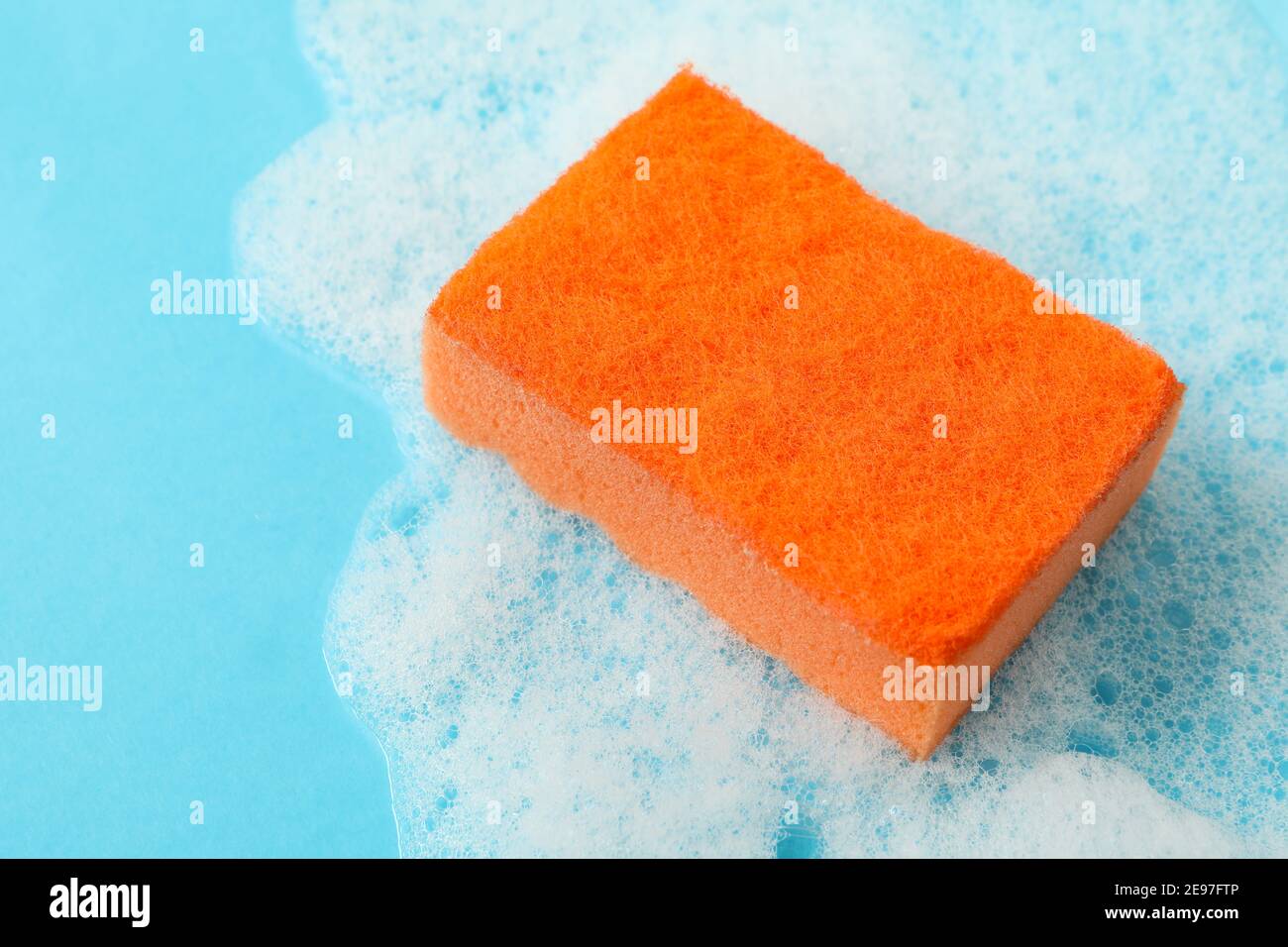 Orangefarbener Schwamm und Schaumstoff auf blauem Hintergrund Stockfoto