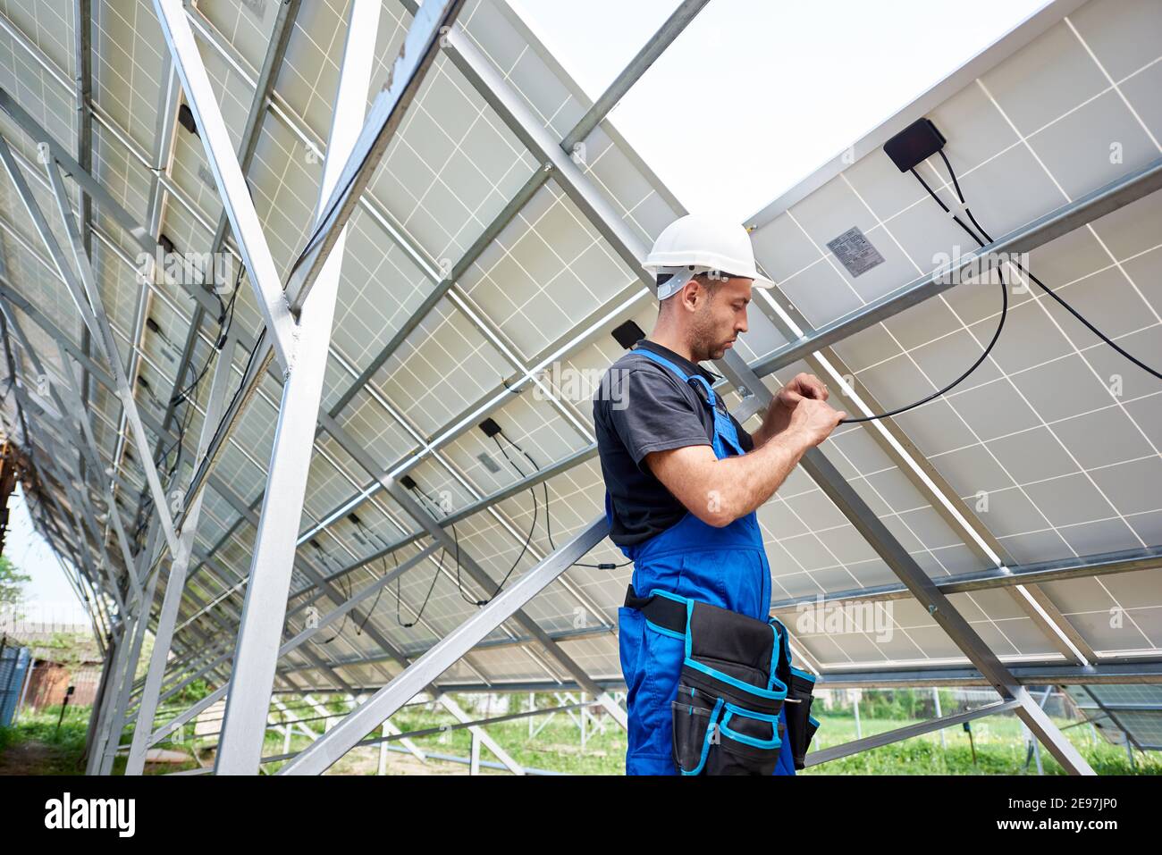 Junge Ingenieur Techniker macht elektrische Verkabelung stehen innerhalb hohe außen Solarpanel Foto voltaic System an hellen sonnigen Sommertag. Umweltfreundliche billige Stromerzeugung Konzept. Stockfoto