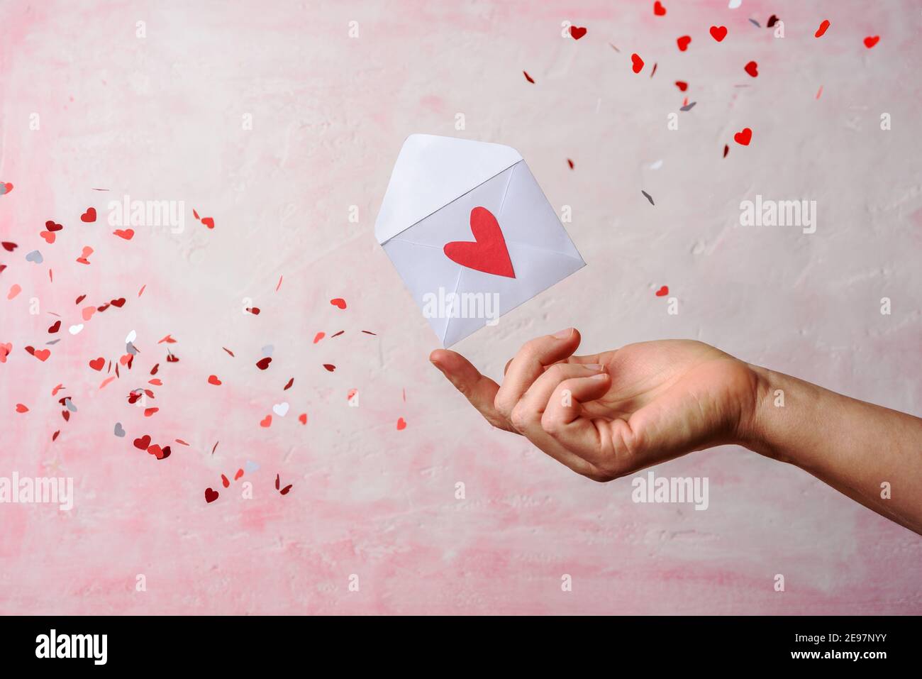 Umschlag auf der Hand mit fliegenden roten Herzen auf rosa Hintergrund. Valentinstag Stockfoto