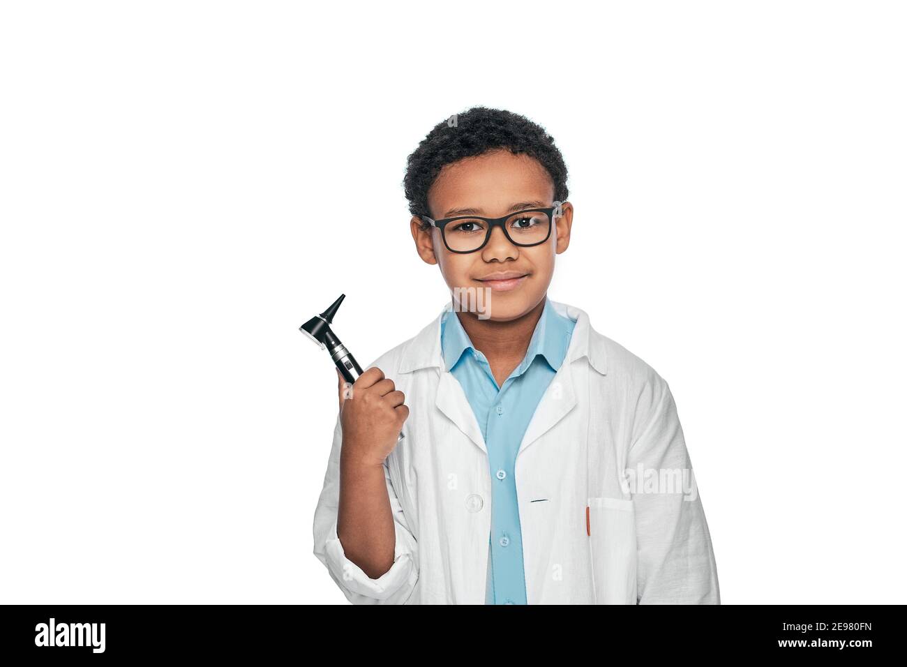 Afroamerikanischer Junge trägt medizinische Uniform hält Otoskop und schaut in die Kamera. Ohrbehandlung und Hörtest für Kinder Stockfoto