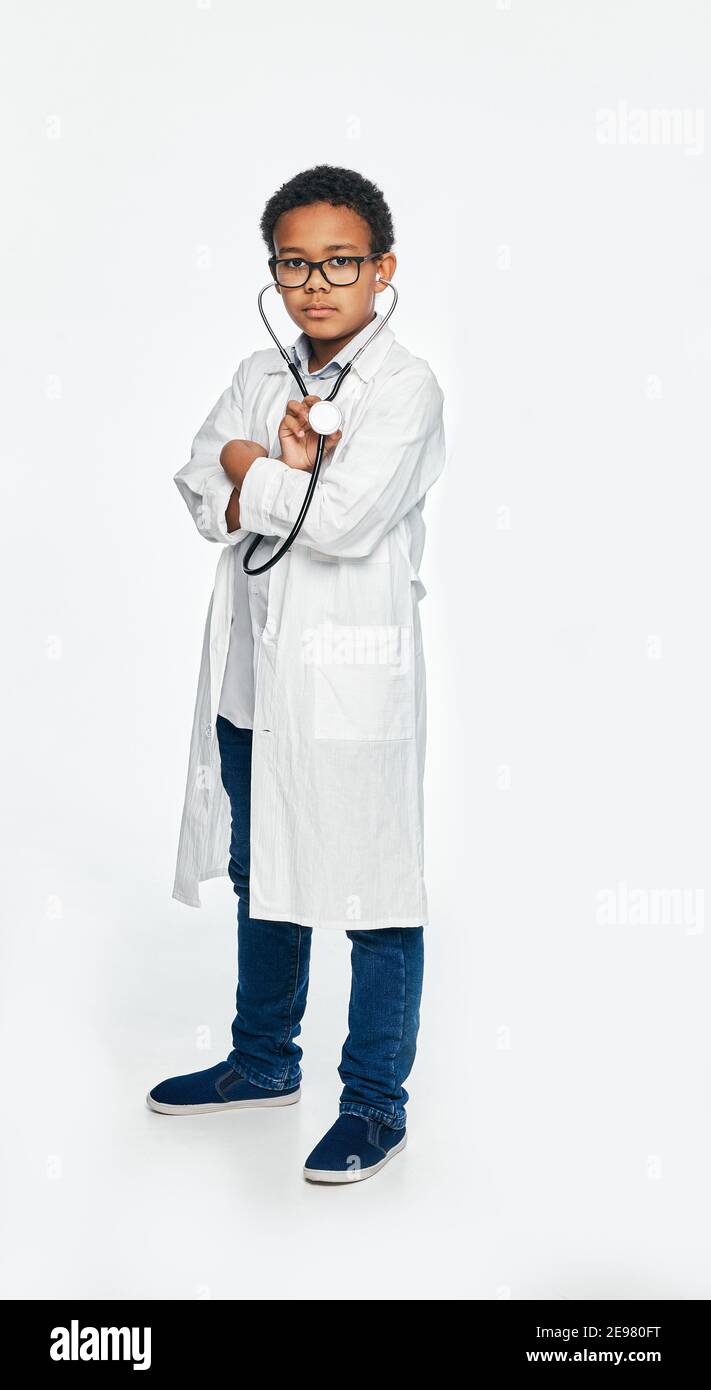 Serious afroamerikanischen Jungen trägt einen Arzt Mantel mit Arm gekreuzt, posiert und Blick auf die Kamera, voller Länge Stockfoto