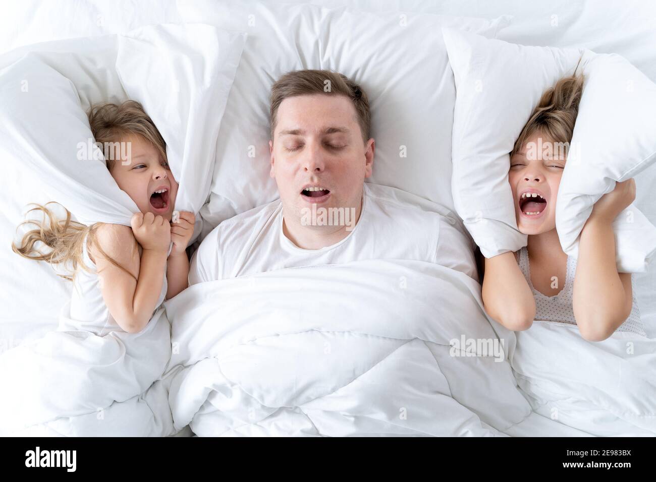 Kinder, Papa schlafen zusammen im Bett. Vater schnarcht hart, Mädchen, Töchter bedecken die Ohren mit Kissen. Störungen, Gelenkschlaf. Schlaflosigkeit, Nacht Stockfoto