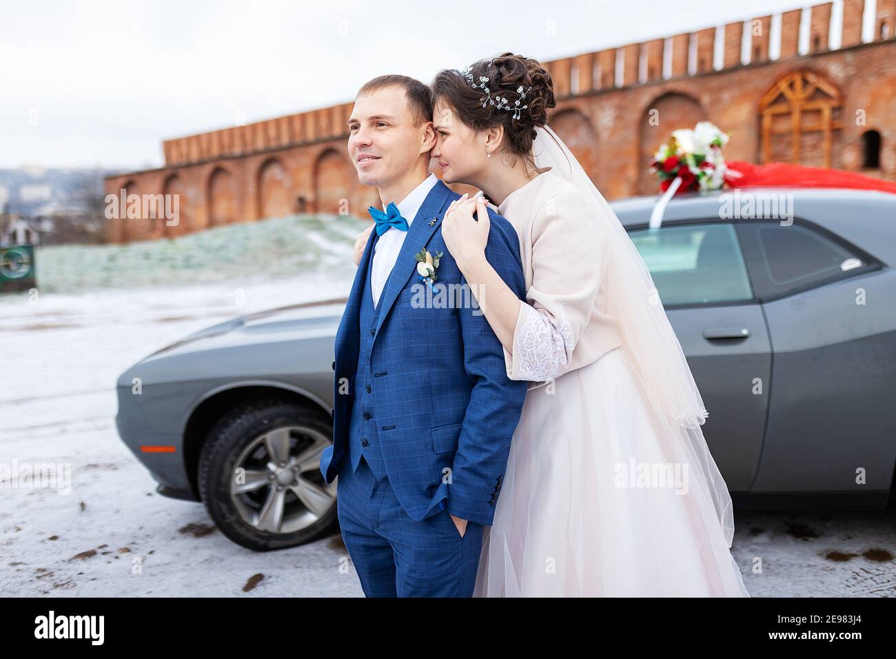 Die Braut und der Bräutigam in der Nähe des Autos, umarmen und küssen ihre Liebsten bei der Hochzeit, die Familie beim Winterfotoschießen mit der Hochzeitskortege Stockfoto