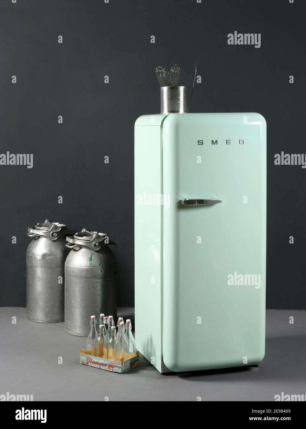 Kit aus Glasflaschen und Aluminiumdosen in der Nähe von kleinen platziert Hellgrüner Retro Smeg Haushaltskühlschrank gegen graue Wand Stockfoto