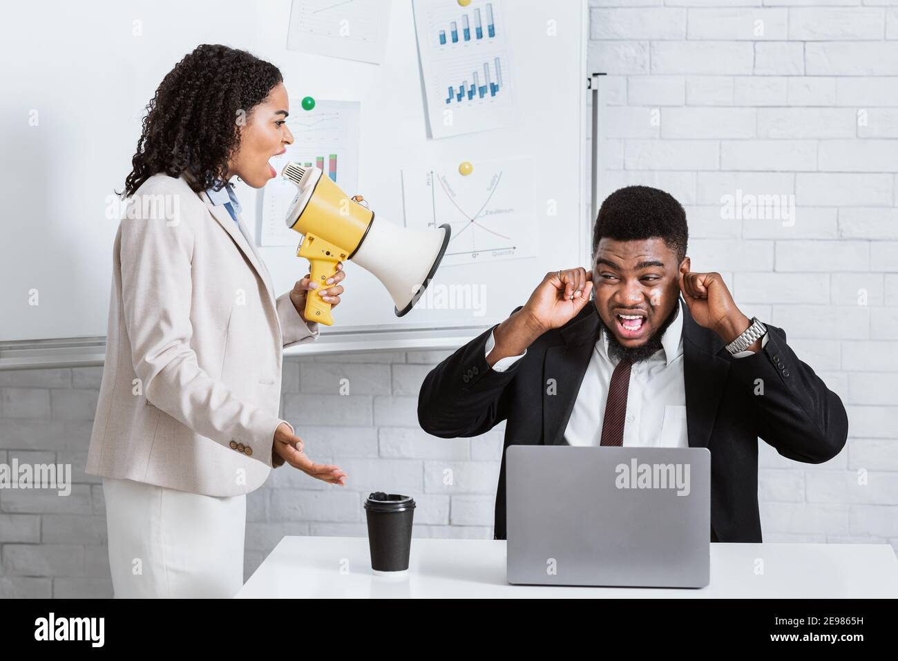 Erzürnte weibliche Chefin mit Lautsprechern, die ihren verängstigten Untergebenen anschreien Im Büro des Unternehmens Stockfoto