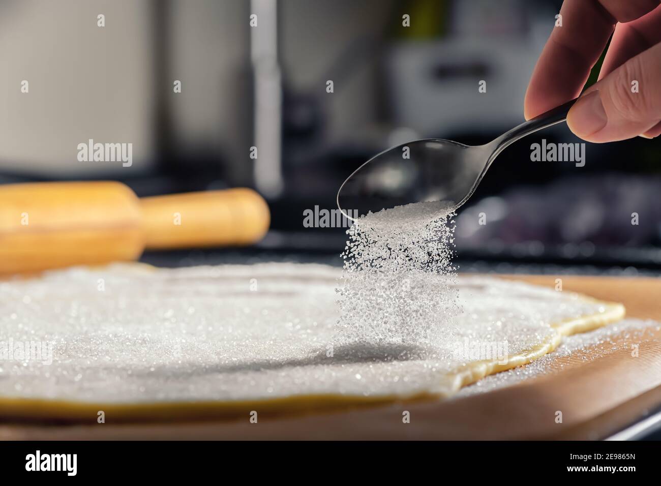 Hand streut Zuckerteig auf dem Tisch. Hausmannskost Stockfoto