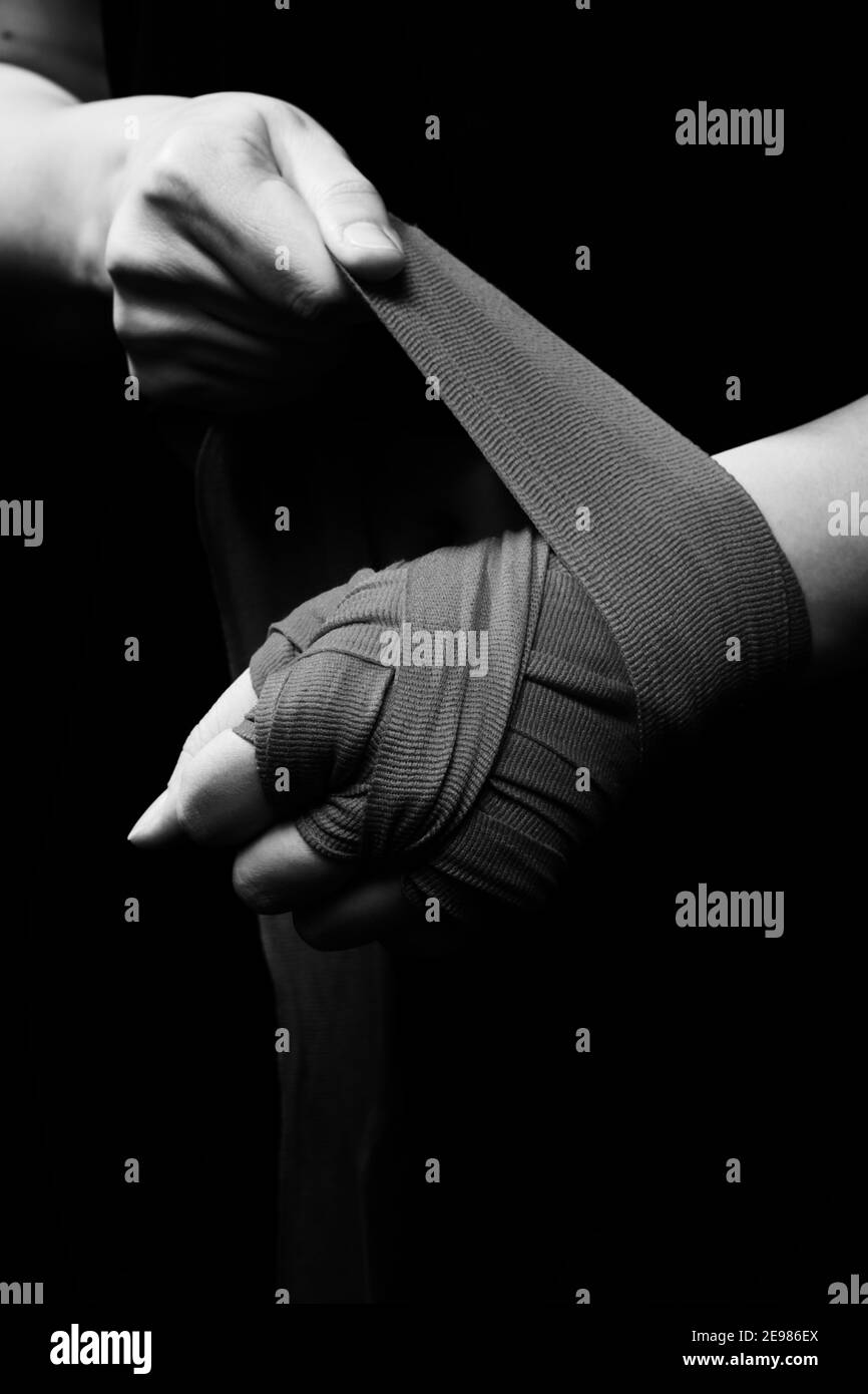 Muay Thai Boxerin mit Trageschlaufe am Handgelenk Nahaufnahme. Fitness junge Frau Vorbereitung für das Boxtraining auf schwarzem Hintergrund, monochrom Stockfoto