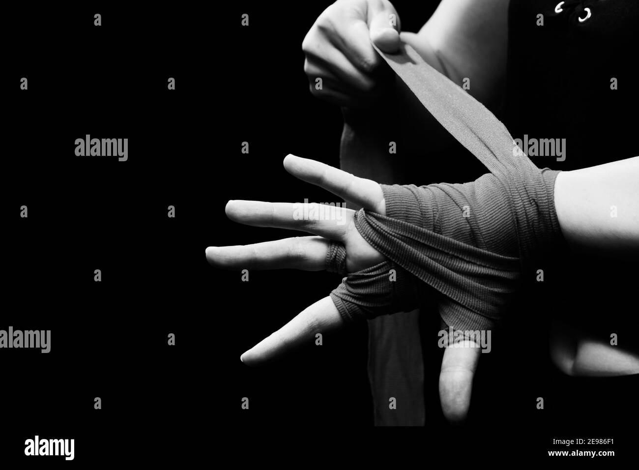 Muay Thai Boxerin mit Trageschlaufe am Handgelenk Nahaufnahme. Fitness junge Frau Vorbereitung für das Boxtraining auf schwarzem Hintergrund, monochrom Stockfoto