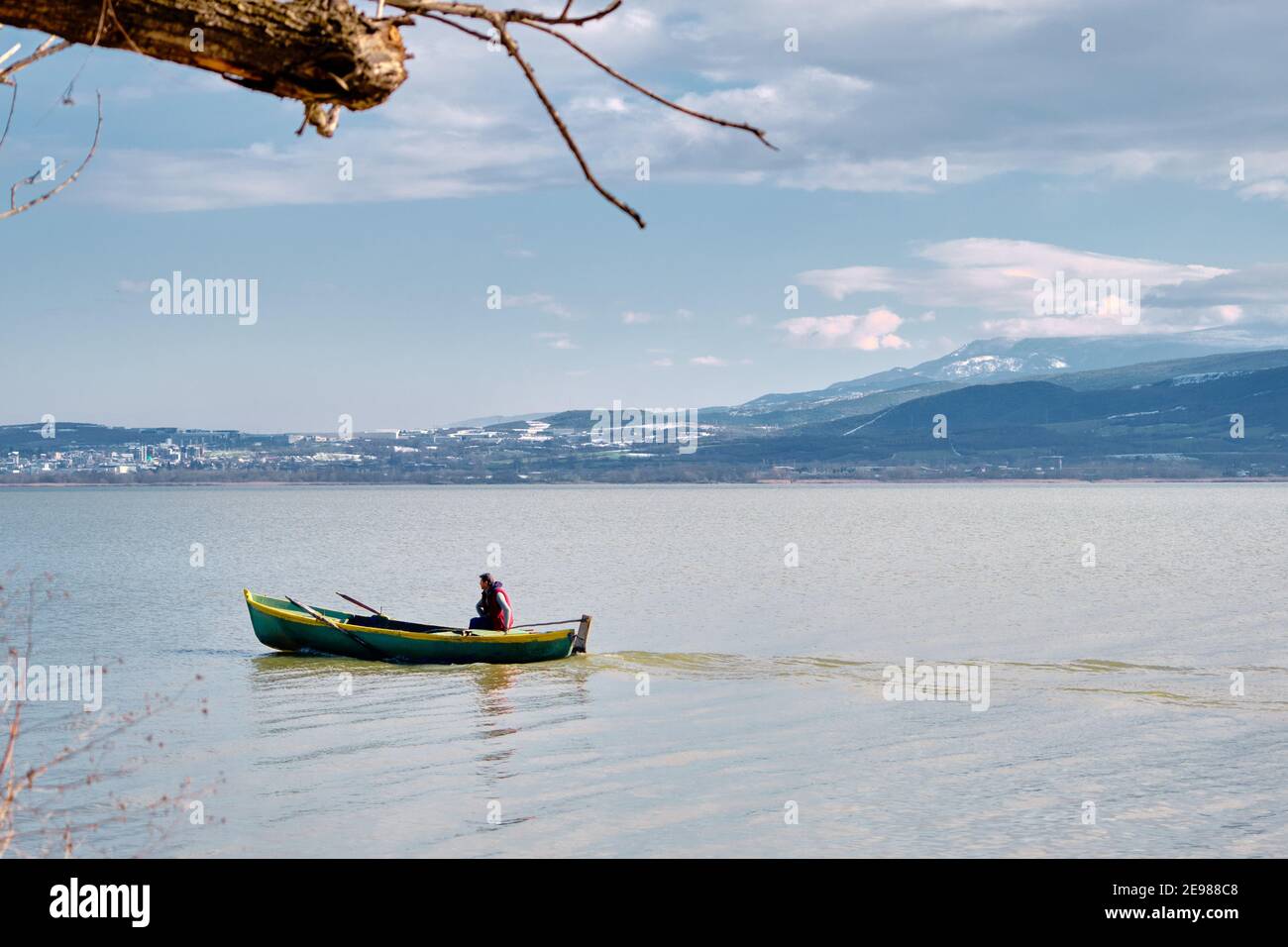 Mann auf dem kleinen und alten Boot im See von Uluabat mit riesigen Berghintergründen. Golyazi. Bursa. Türkei. Stockfoto