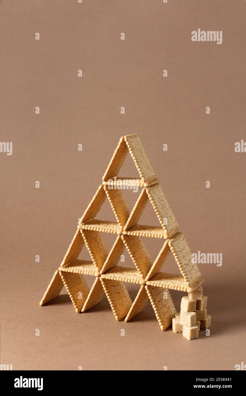 Stillleben der kreativen Komposition mit quadratischen Cookie in Form von Dreieck mit Stücken von braunem Zucker ausgeglichen. Stockfoto