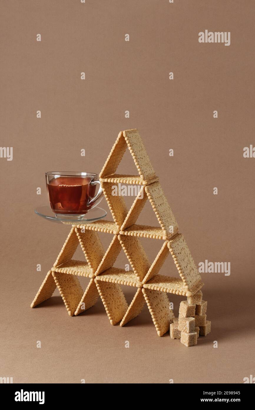 Stillleben der kreativen Komposition mit Cookie und Tasse Tee in Form von Dreieck mit Stücken von braunem Zucker ausgeglichen. Stockfoto