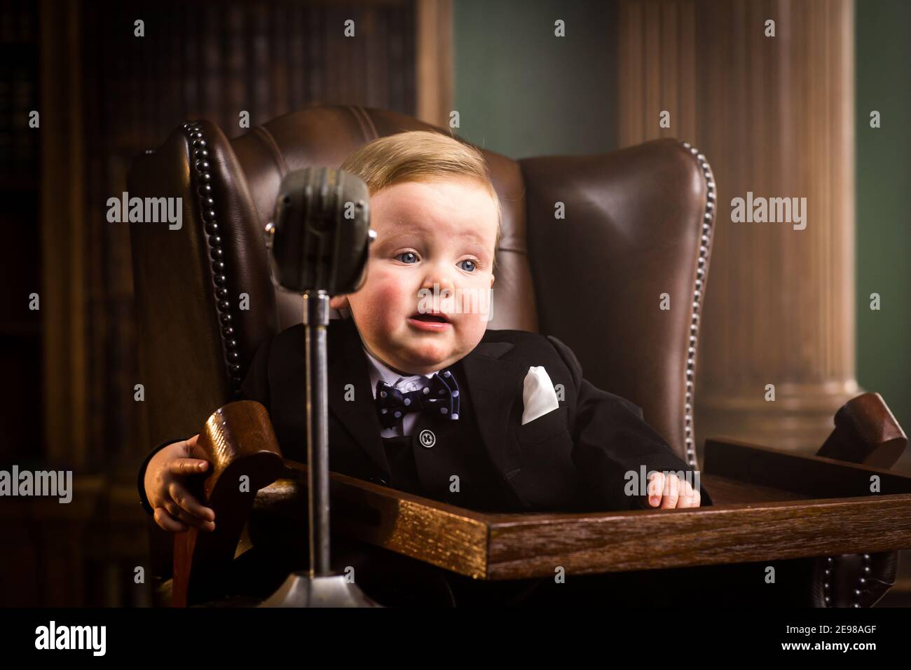 Happy Baby in Business-Anzug gekleidet. Kleinkind als Winston Churchill gekleidet saß in Leder Nietenstuhl mit Live-Übertragung Radio-Mikrofon. Stockfoto