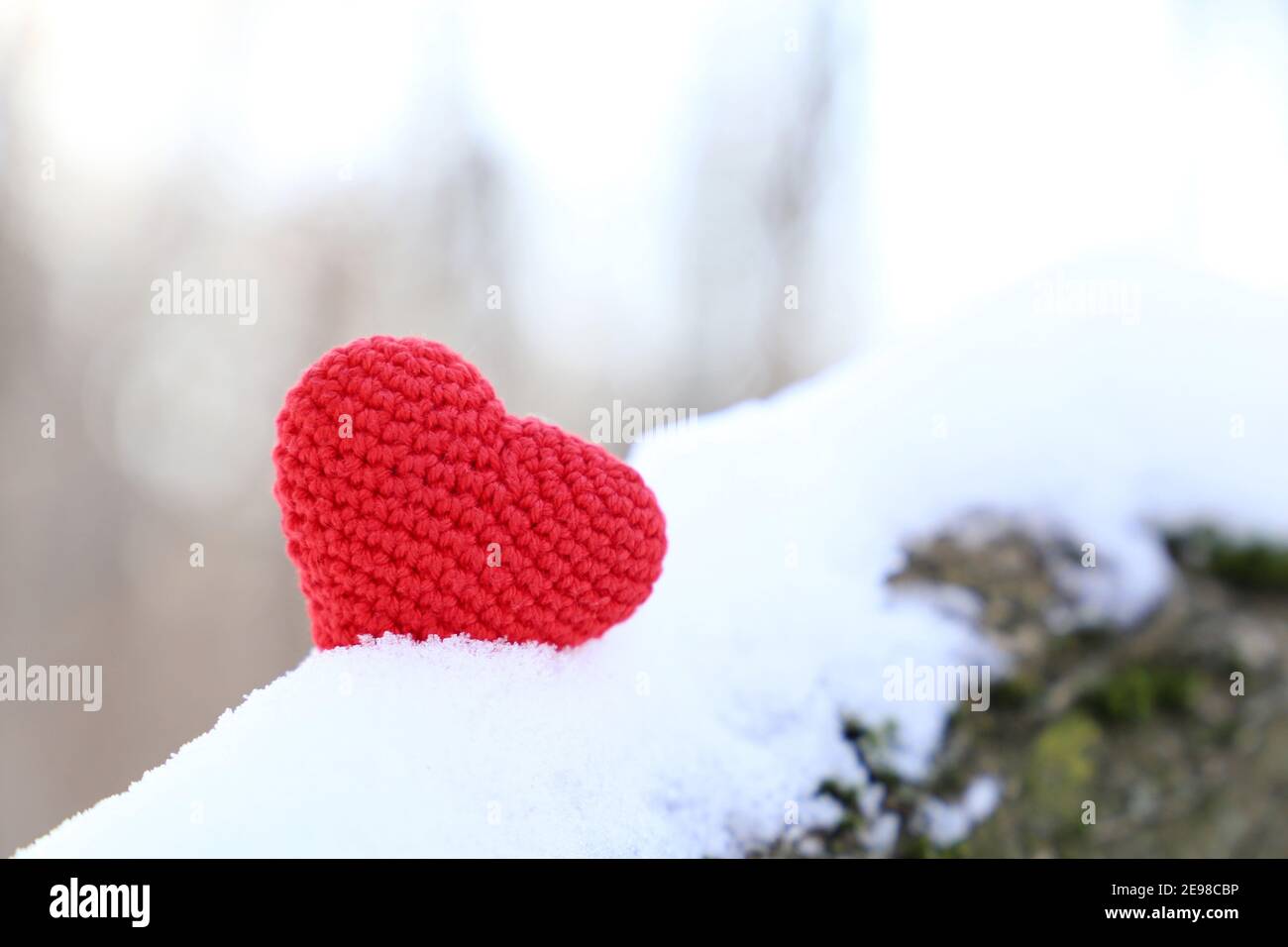 Valentine Herz auf dem Schnee im Sonnenlicht. Rot gestricktes Symbol der romantischen Liebe auf einem Zweig im Winterwald, Hintergrund für den Urlaub Stockfoto