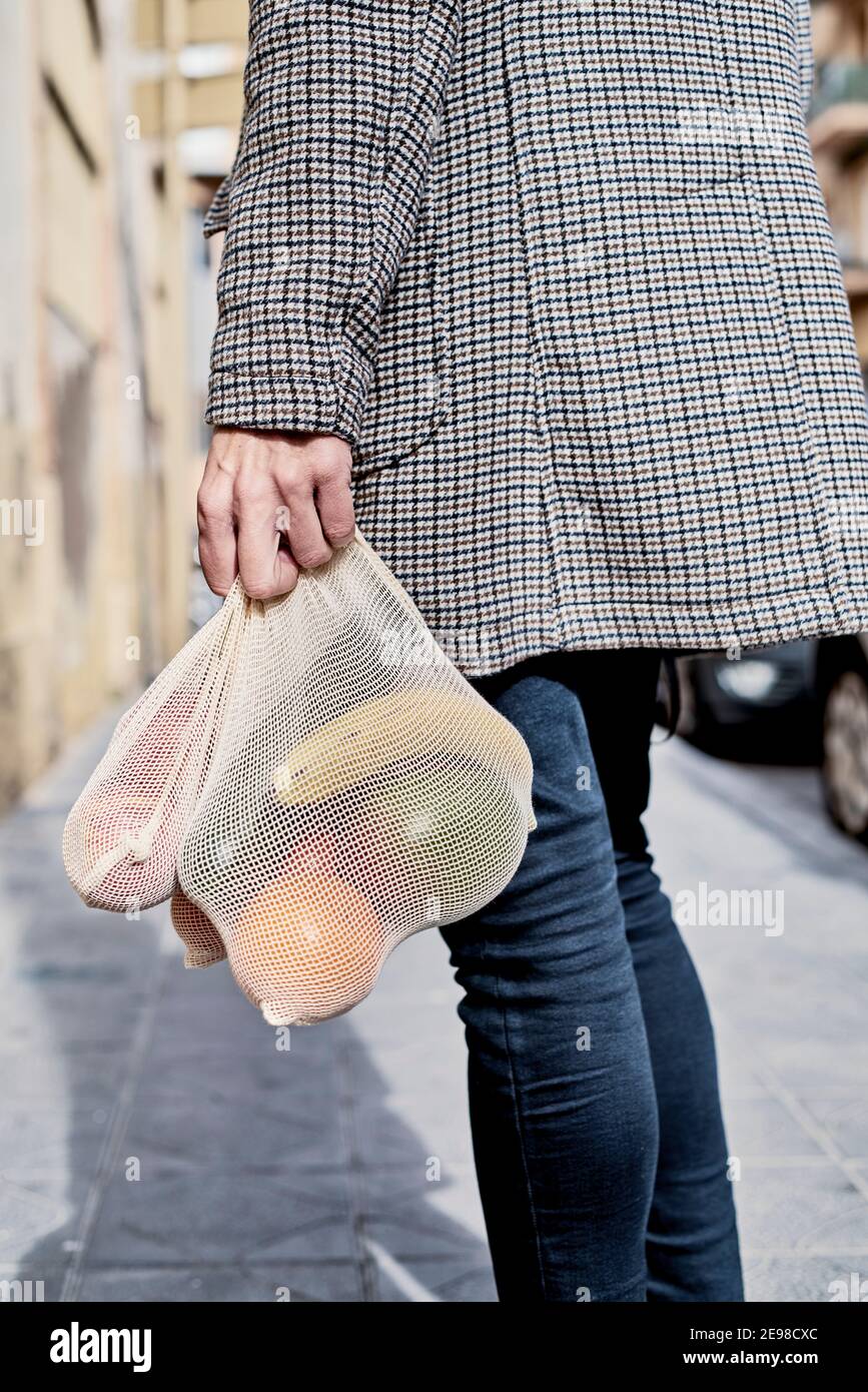 Nahaufnahme eines Mannes auf der Straße, von hinten gesehen, mit einem Textil wiederverwendbaren Netzbeutel, verwendet, um Lebensmittel in großen Mengen zu kaufen, voller Obst und Gemüse, ein Stockfoto