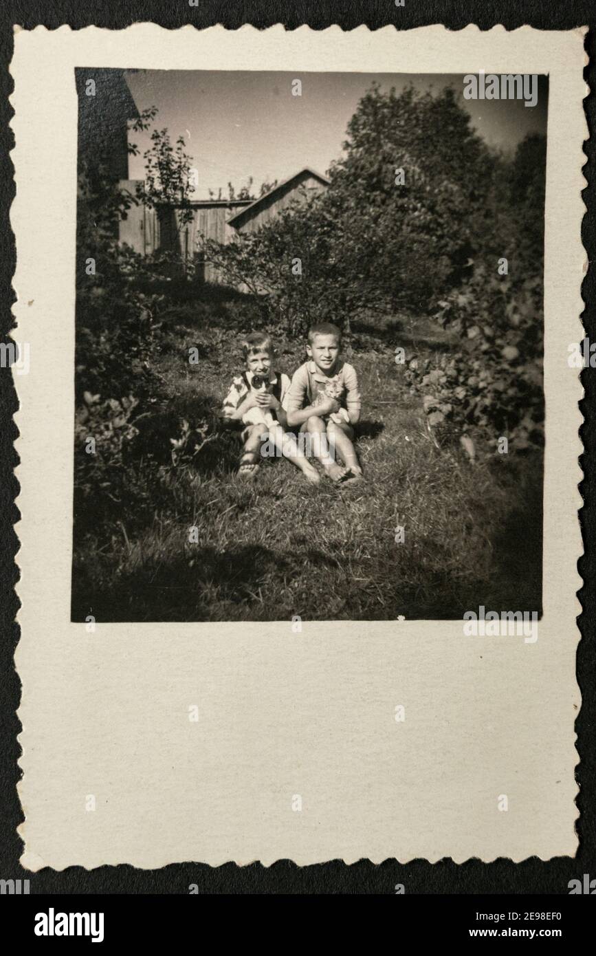 Deutschland - UM 1930s: Gruppenfoto von zwei kleinen Kindern, die im Garten sitzen und Katzen halten. Vintage Archiv Art Deco Ära Fotografie Stockfoto