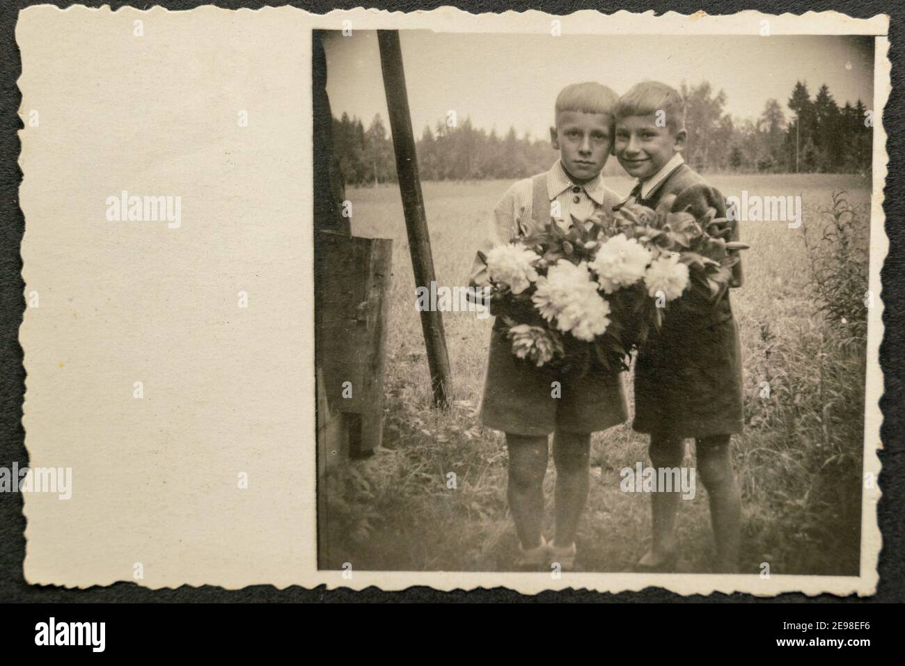 Deutschland - UM 1930s: Zwei kleine Kinder stehen und halten Blumen im Garten. Vintage Archiv Art Deco Ära Fotografie Stockfoto