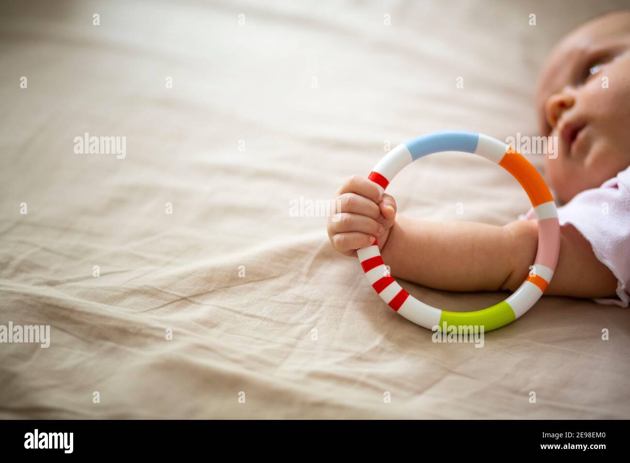 Detail der Hand eines Neugeborenen, der ein buntes Spielzeug-Rad hält. Beigefarbener Hintergrund. Gesicht nicht fokussiert. Stockfoto