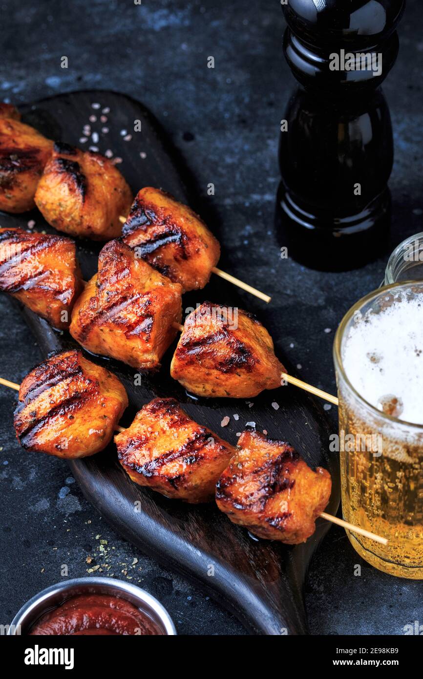 Einfach und lecker Chicken Kebabs. Gegrilltes Hähnchen auf Bambusspießen mit einem Getränk. Dunkler Hintergrund. Stockfoto