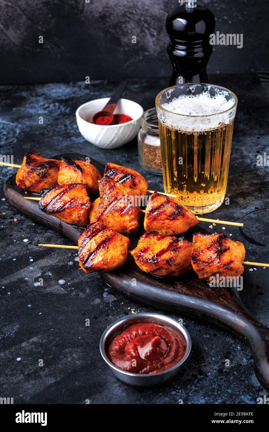 Einfach und lecker Chicken Kebabs. Gegrilltes Hähnchen auf Bambusspießen mit einem Getränk. Dunkler Hintergrund. Stockfoto