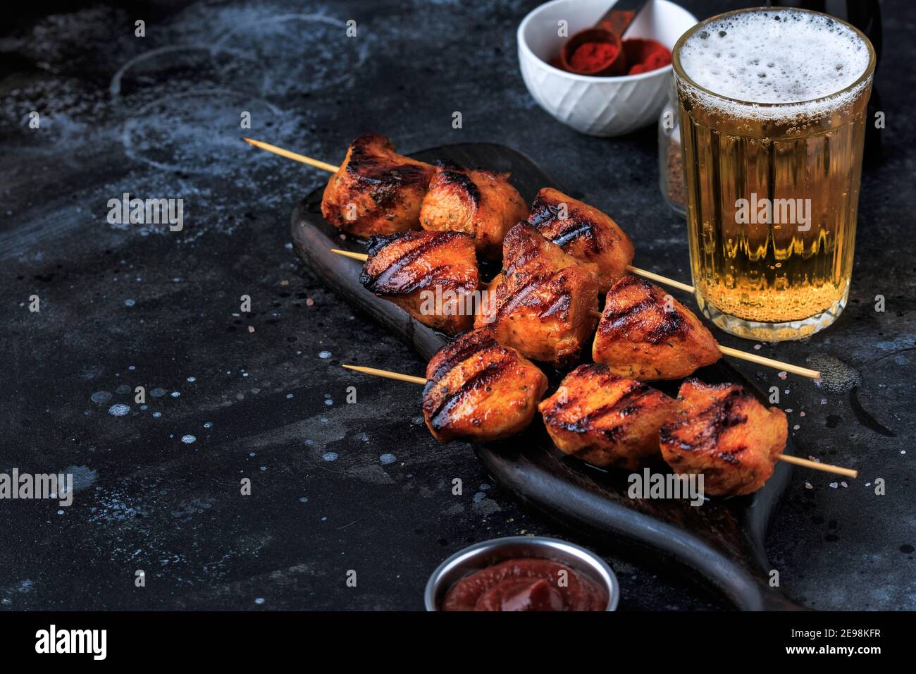 Einfach und lecker Chicken Kebabs. Gegrilltes Hähnchen auf Bambusspießen mit einem Getränk. Dunkler Hintergrund. Stockfoto