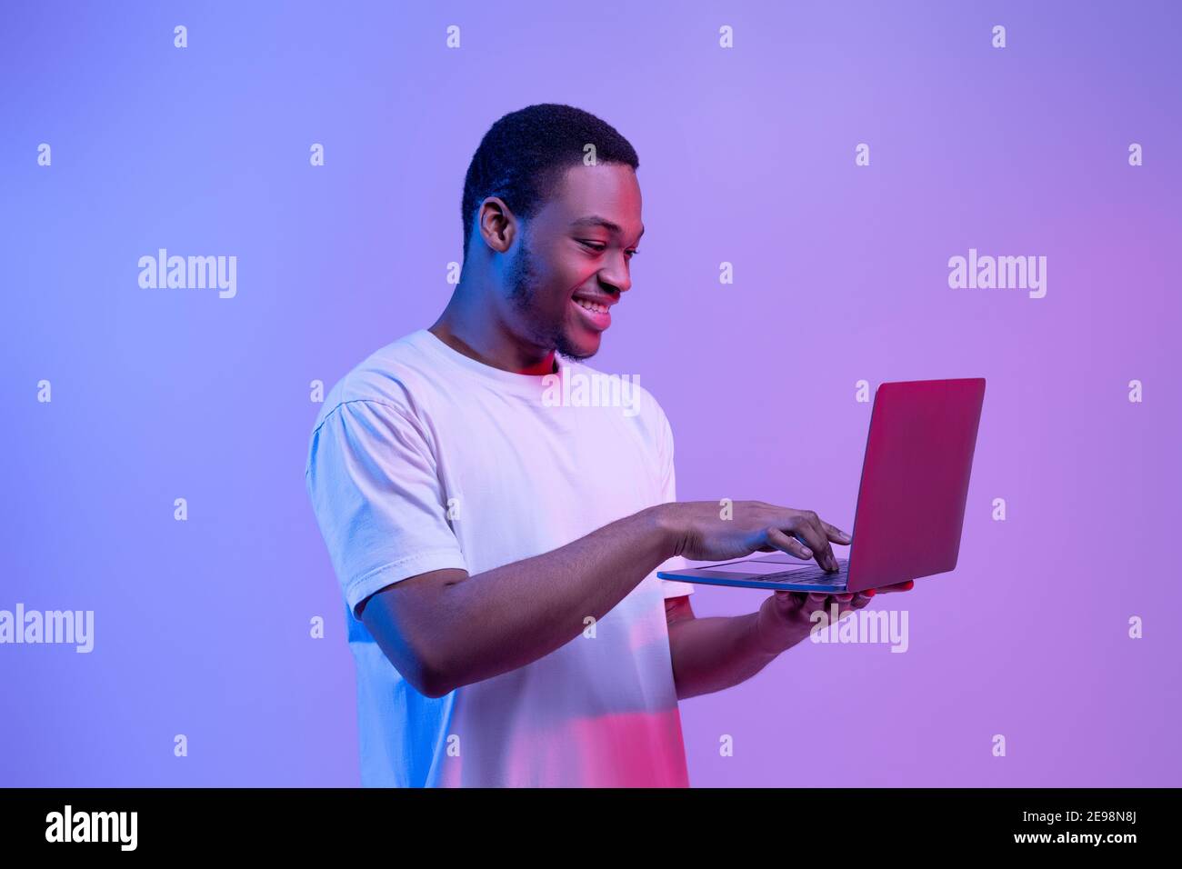Moderne Technologien. Happy Black Man Mit Laptop-Computer In Neon Licht Stockfoto