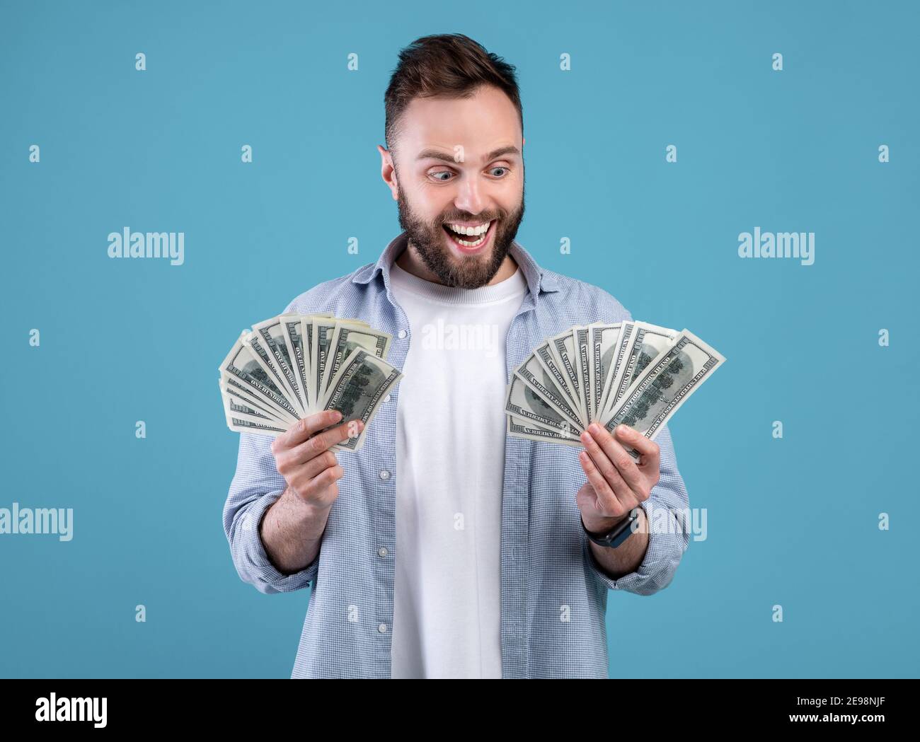 Wohlhabender Kaukasischer Kerl mit zwei Fans auf Geld begeistert über seinen großen Erfolg über blauen Hintergrund. Riesiges Gewinnkonzept Stockfoto