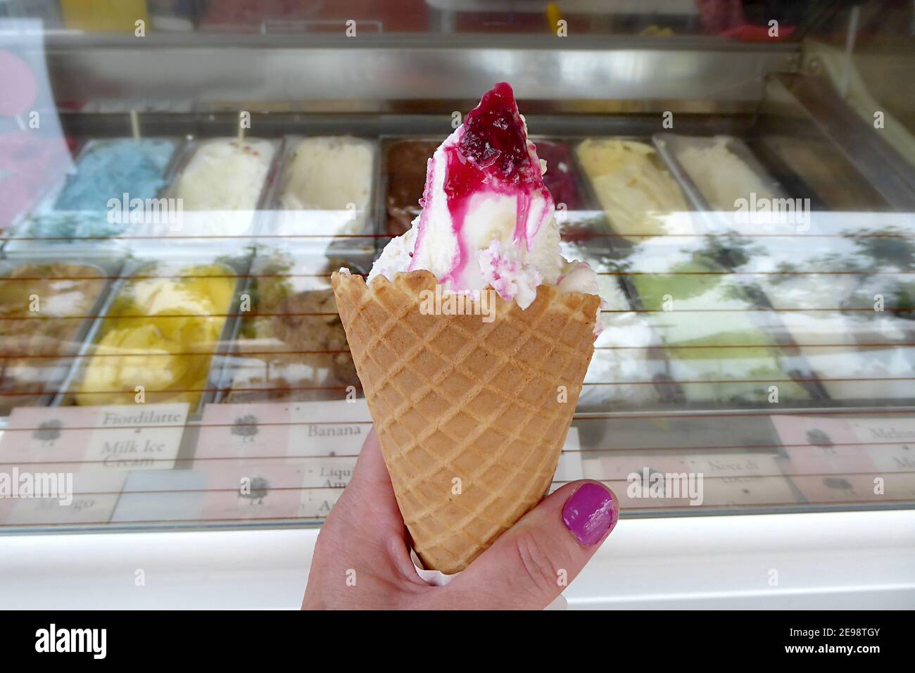 Eine Frauenhand mit einem einzigen Eiskegel gefüllt mit renommierten italienischen Gelato gekrönt mit runny schwarzen Kirsch-Sauce, aus einer Vielzahl von Fla ausgewählt Stockfoto
