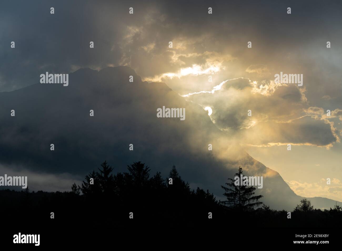 Die Sonne kommt hinter Wolken über Baumkronen hervor Stockfoto