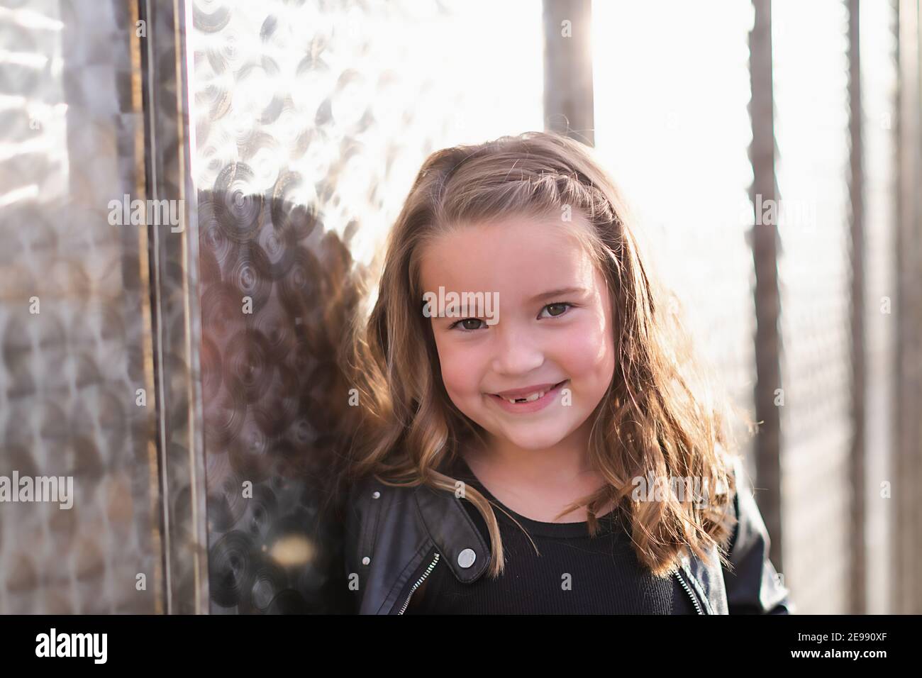 Lächelndes junges Mädchen mit Grübchen, die an einer Metallwand gelehnt sind. Stockfoto