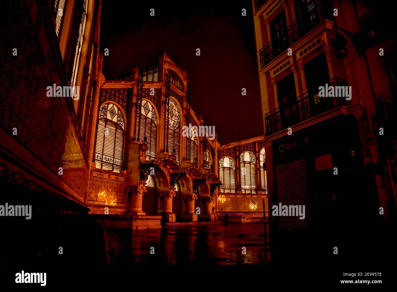 Fassade des Jugendstilmarktes 'Mercat Central' beleuchtet von innen in der Nacht mit nassen Straße in Valencia, Spanien Stockfoto