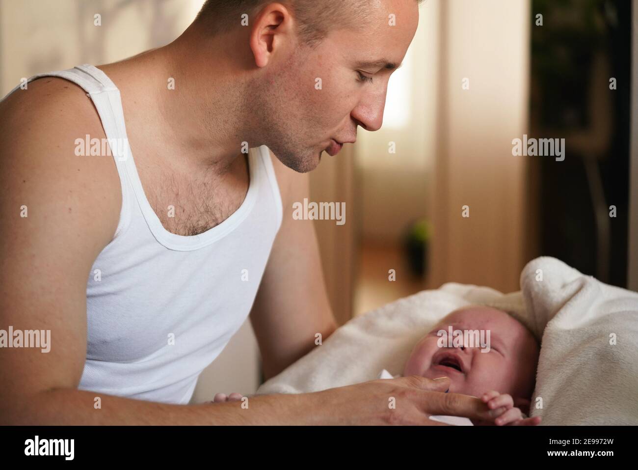 Junger Mann trägt nur Weste Top, spielt mit seinem kleinen Sohn, versucht, sich zu beruhigen, schreiende Kind, wie er hält ihn an den Händen Stockfoto