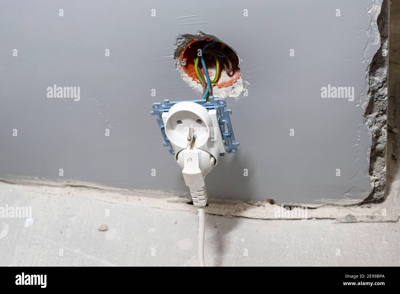 Doppelte Steckdose, die aus der Wand herausragt und an elektrischen Kabeln befestigt ist. Stockfoto