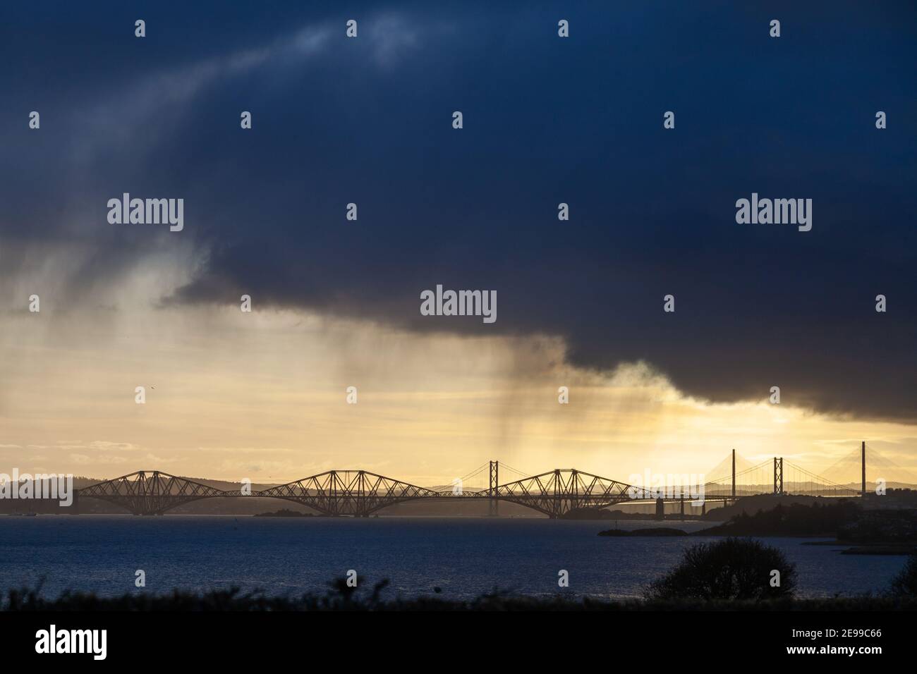 Die Forth Bridges, die zurück beleuchtet werden, als ein Regensturm durch den Firth of Forth geht. Stockfoto