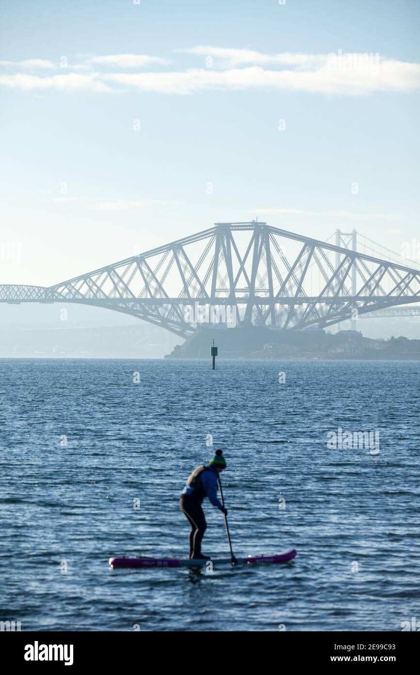 Ein Paddelboarder, der die Wintersonne auf dem Firth of Forth in der Nähe der Forth Bridge in Saint Davids Bay Fife genießt Stockfoto