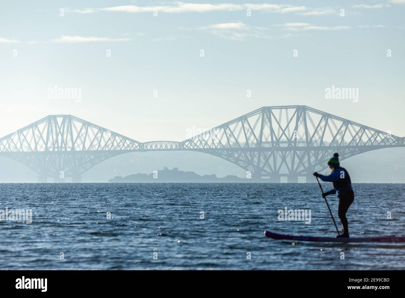 Ein Paddelboarder, der die Wintersonne auf dem Firth of Forth in der Nähe der Forth Bridge in Saint Davids Bay Fife genießt Stockfoto