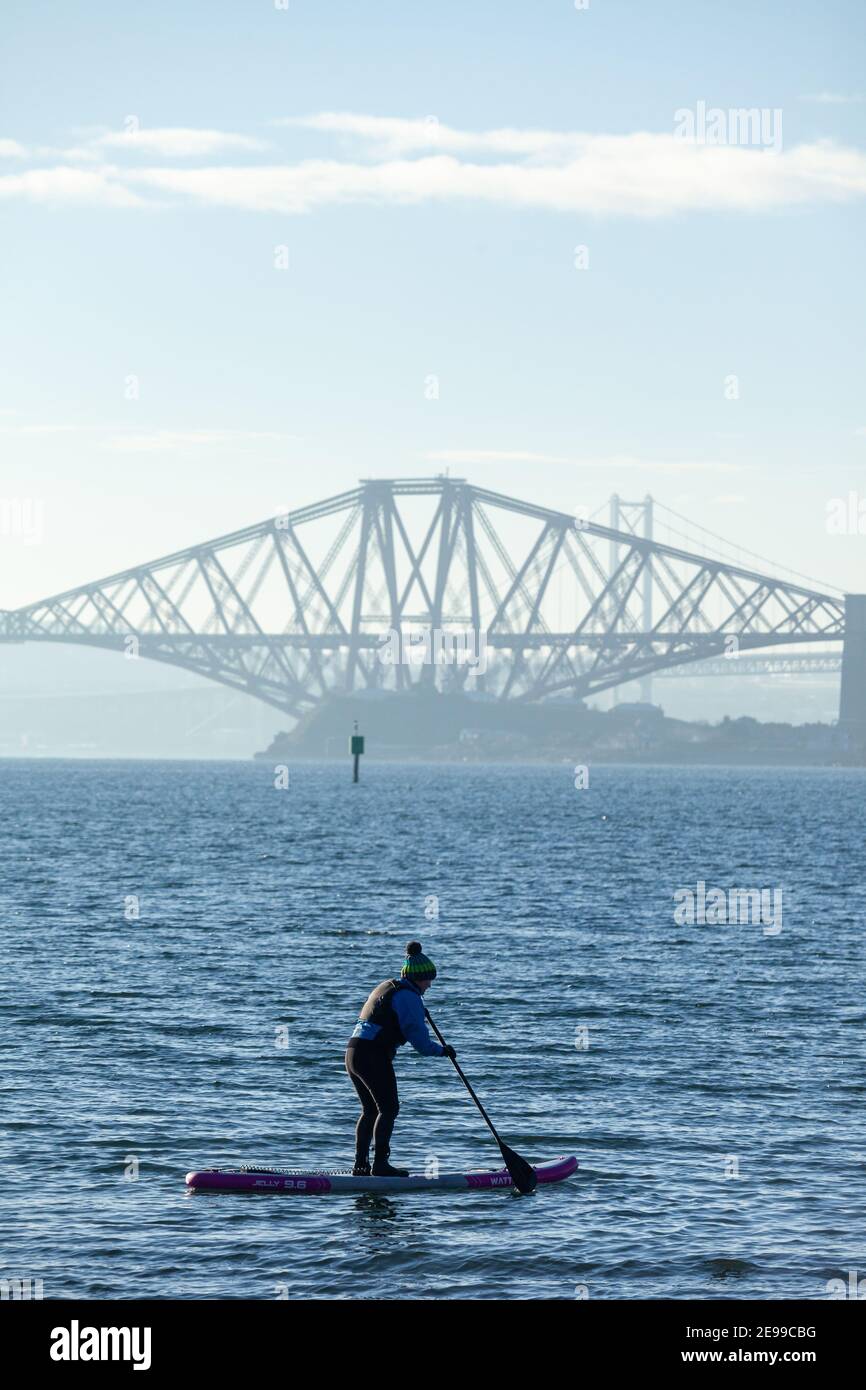 Ein Paddelboarder, der die Wintersonne auf dem Firth of Forth in der Nähe der Forth Bridge in Saint Davids Bay Fife genießt Stockfoto