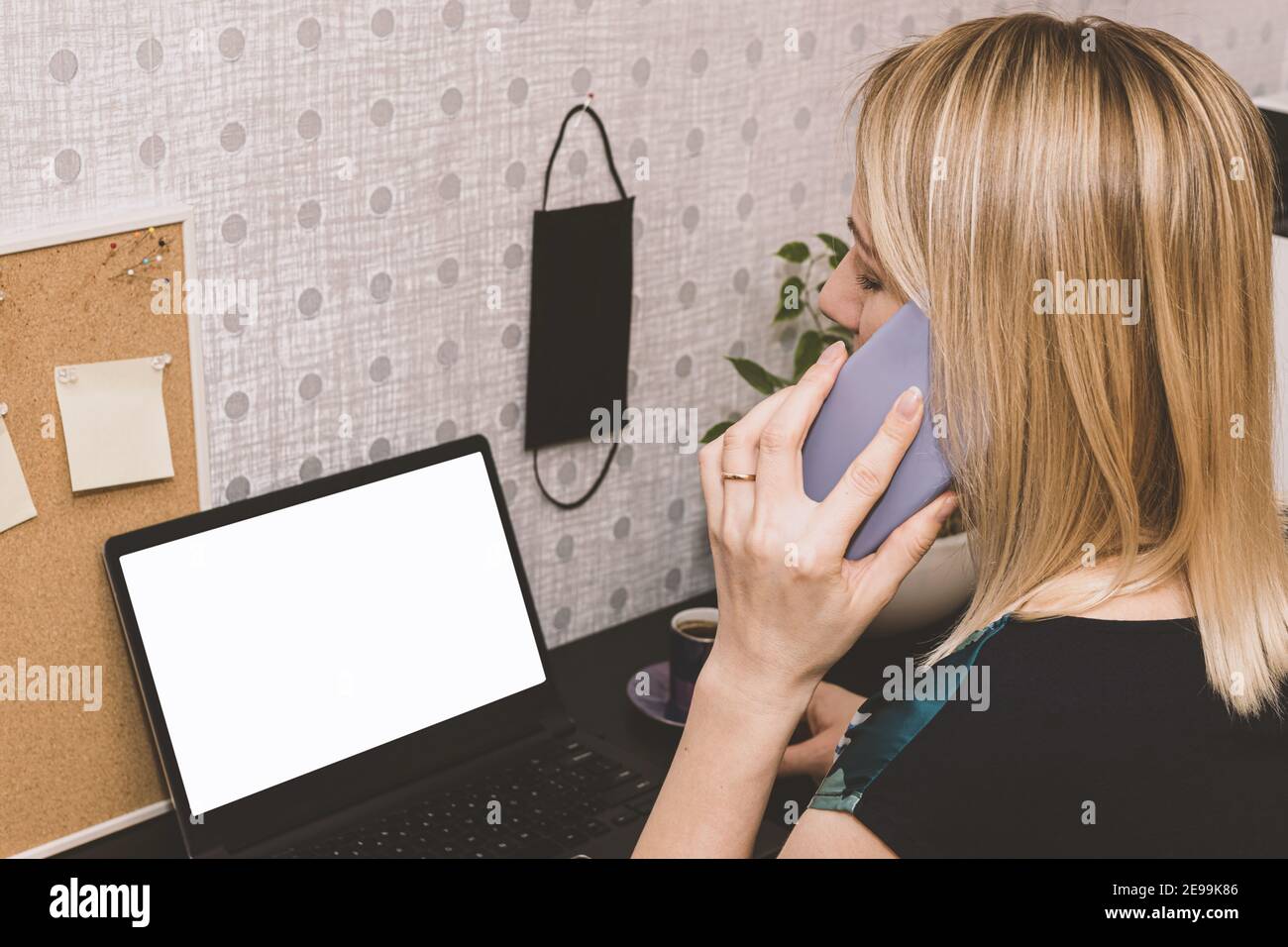 Gesundheitskonzept. Blonde Frau arbeitet mit Computer mit weißem leeren Bildschirm für Kopierraum und sprechen mit Handy von zu Hause aus während Quarantäne Stockfoto