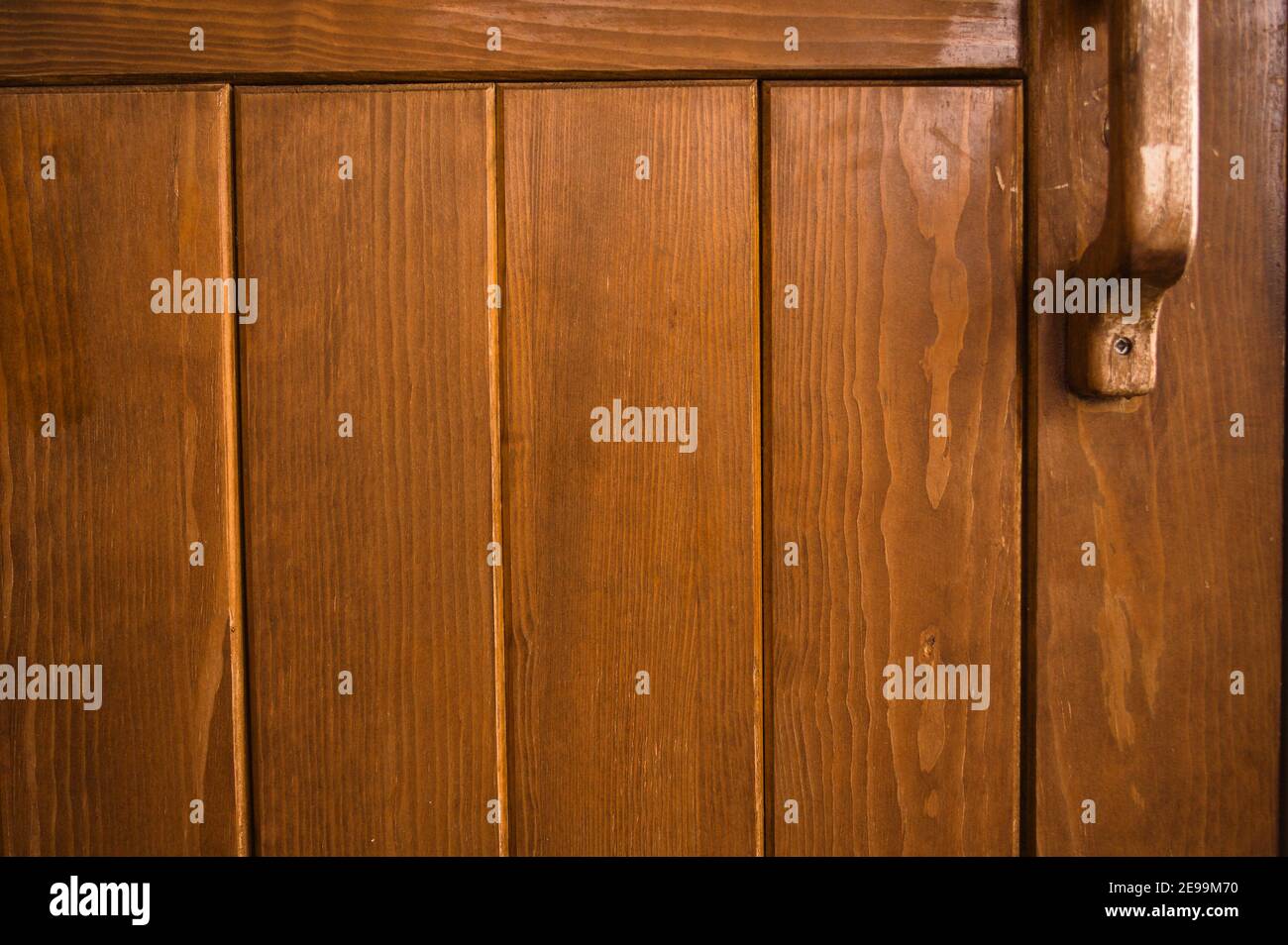 Ein hölzerner Türgriff auf einer schweren Holztür mit gleichmäßig verteilten, reichen braunen Paneelen. Stockfoto