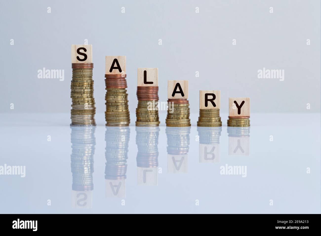 Wort „GEHALT“ auf Holzblöcken auf absteigenden Münzstapeln auf Grau. Konzeptfoto von Geldverlust, Wirtschaftskrise, Rezession und Scheitern. Stockfoto