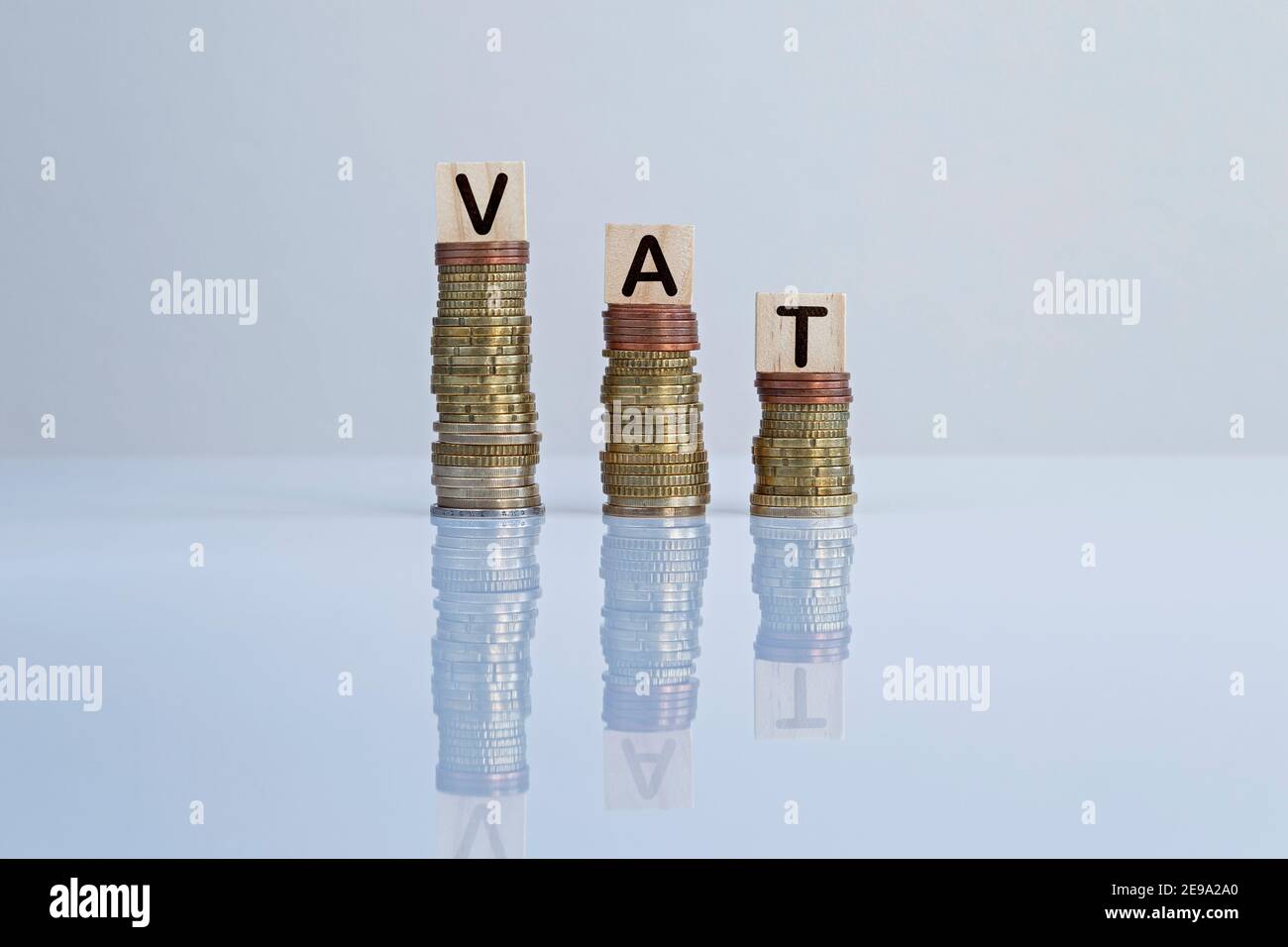 Wort „MwSt.“ auf Holzblöcken auf absteigenden Münzstapeln auf Grau. Konzeptfoto der Reduzierung von Mehrwertsteuer, Wirtschaft, Unternehmen und Finanzen Stockfoto