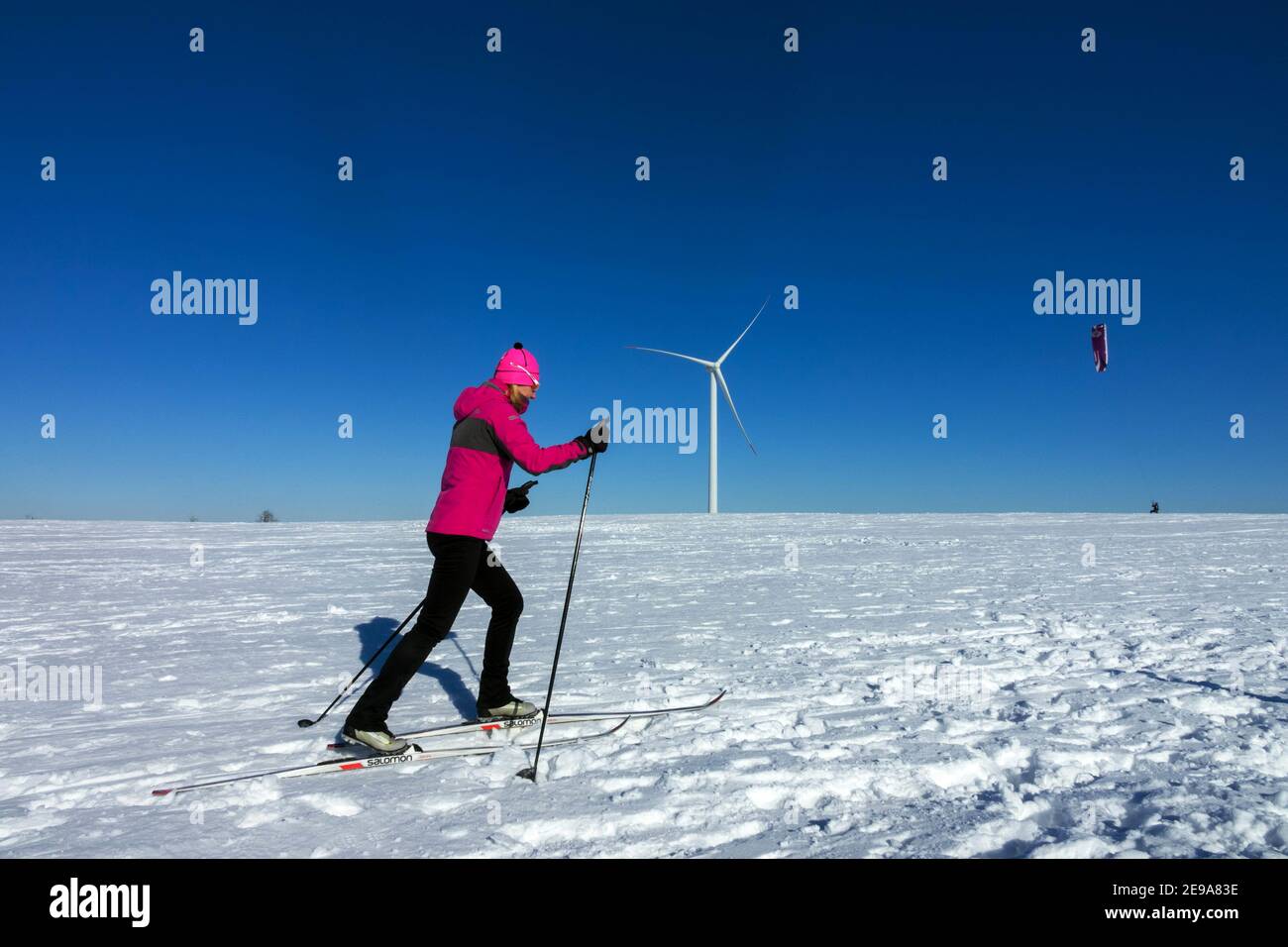 Wintersport, Frau Skilanglauf, und Hintergrund Mann Snowkiten unter einer Windturbine Tschechische Republik Berge Ebene Frau Skifahren Stockfoto