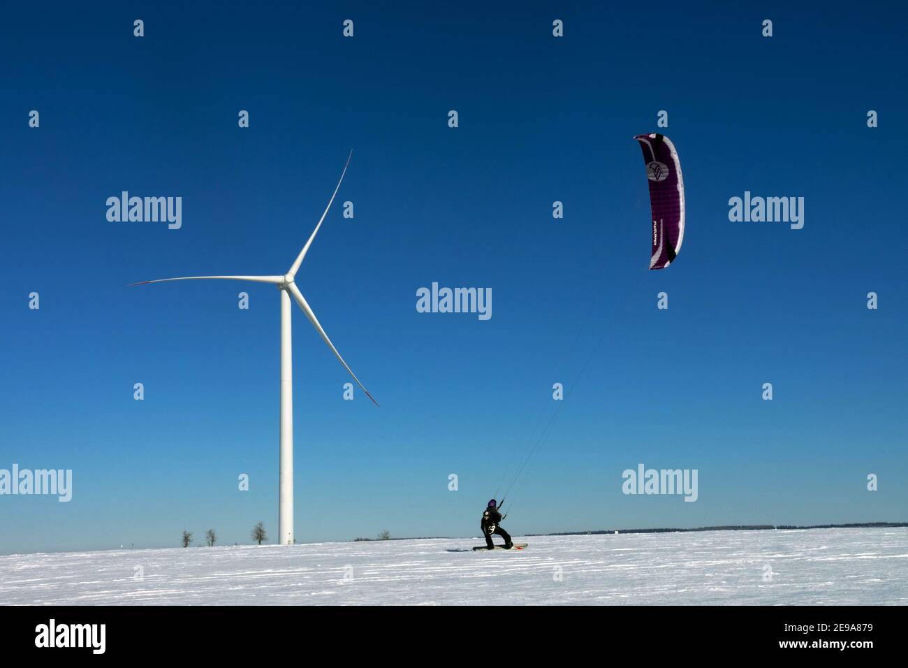 Snowkiten Kiteskiing Mann auf schneebedeckter Ebene mit Windturbine, Windkraft Erzgebirge Tschechien Stockfoto