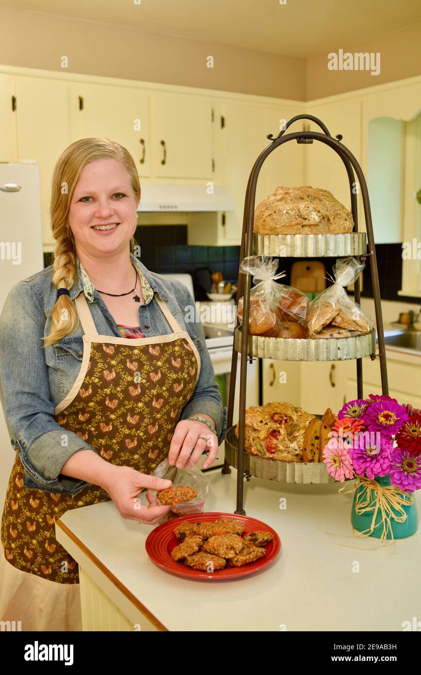 Eine attraktive Erwachsene kaukasische Frau Hausbäcker Putting frische, hausgemachte Kekse in die Tasche, Bake Stand mit Artikeln auf Küchentheke, Wisconsin, USA Stockfoto