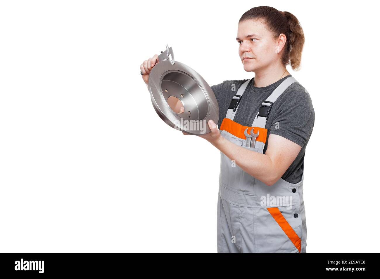 Männlicher Arbeiter in Uniform des arbeitenden Automechanikers mit Schraubenschlüssel Der Schlüssel in der Tasche hält die Bremsscheibe in den Händen und misst die Größe Von Kfz-Ersatzteilen mit Bremssattel t Stockfoto