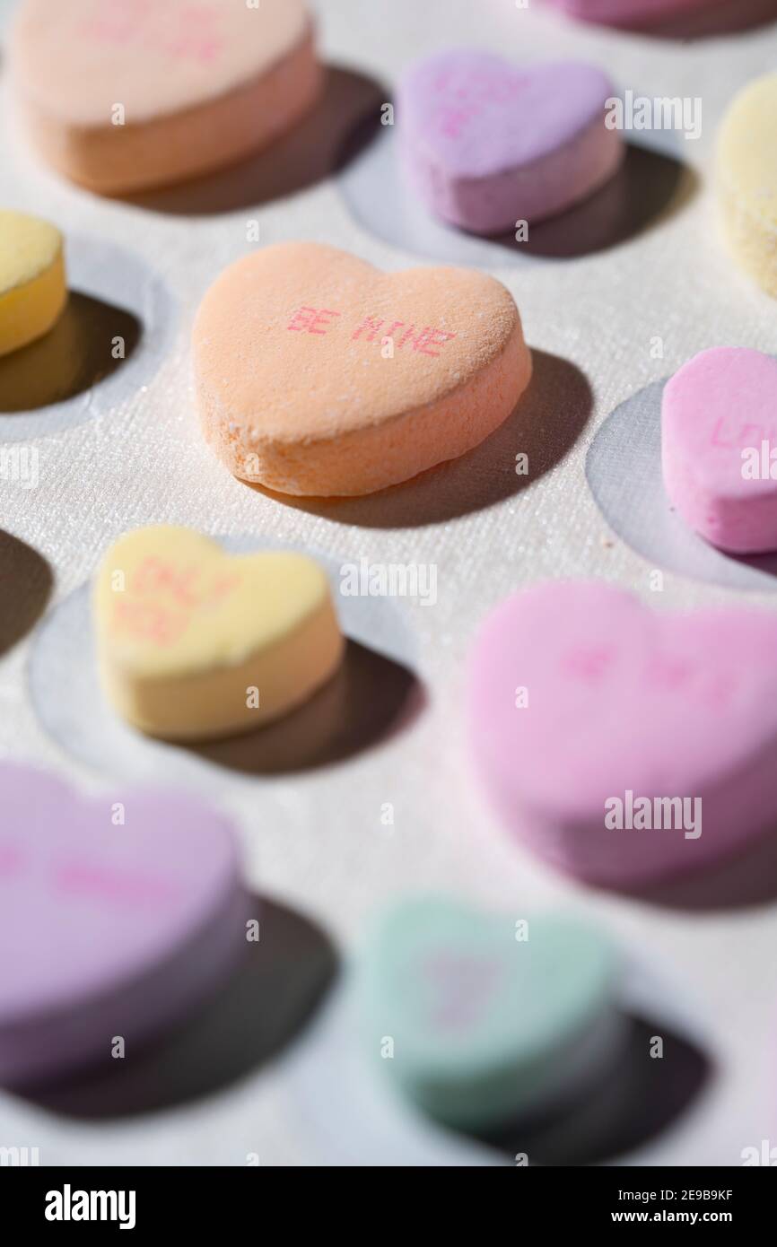 Reihen von bunten Gespräch Süßigkeiten Herzen aufgereiht in Reihen Auf einer weißen Oberfläche mit einem Herzen im Fokus Lesen „Be Mine“ Stockfoto
