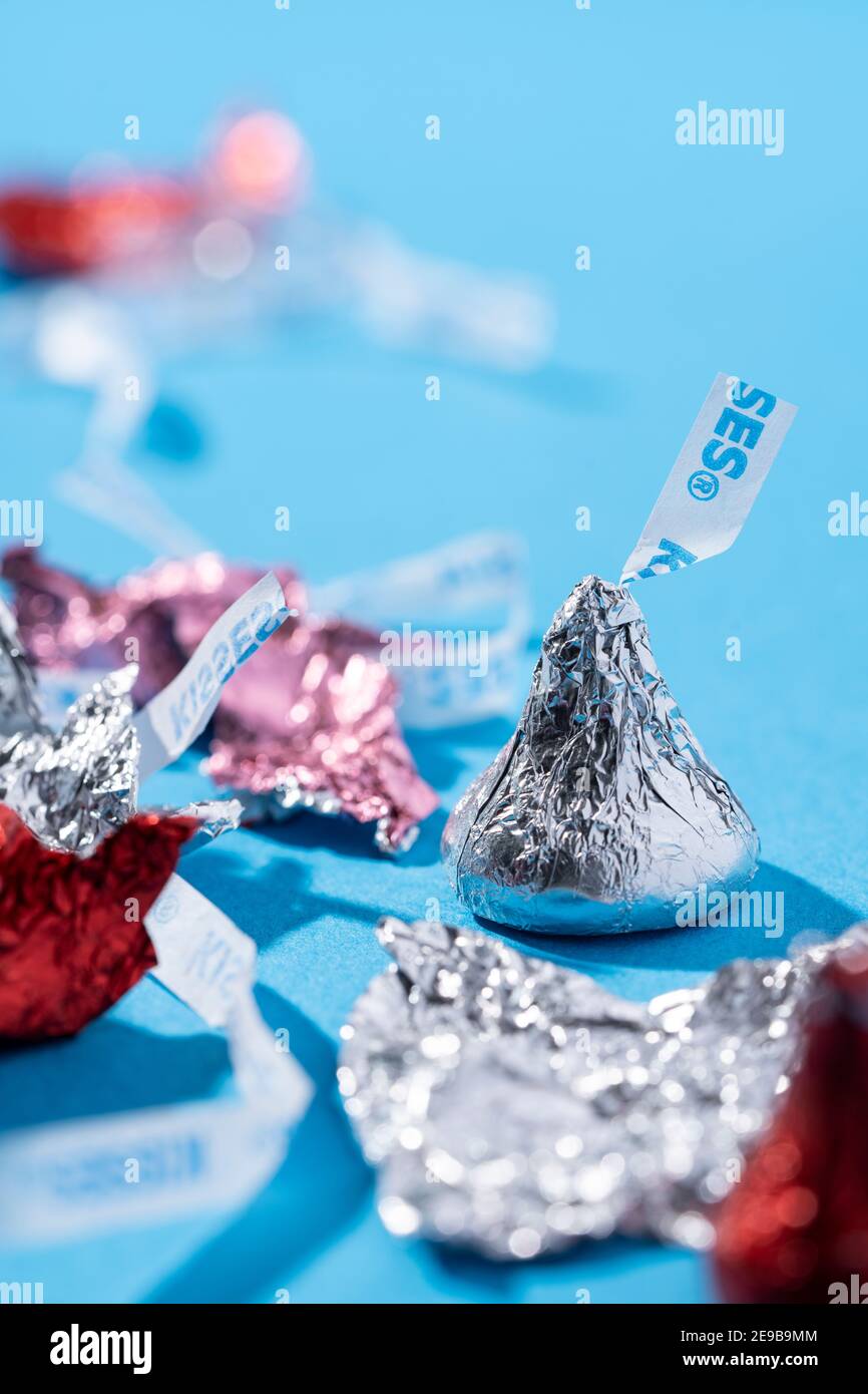 Ein Bündel von eingewickelten Hershey Kisses in roten, rosa und silbernen Verpackungen und leere Verpackungen sitzen auf einer blauen Oberfläche Stockfoto