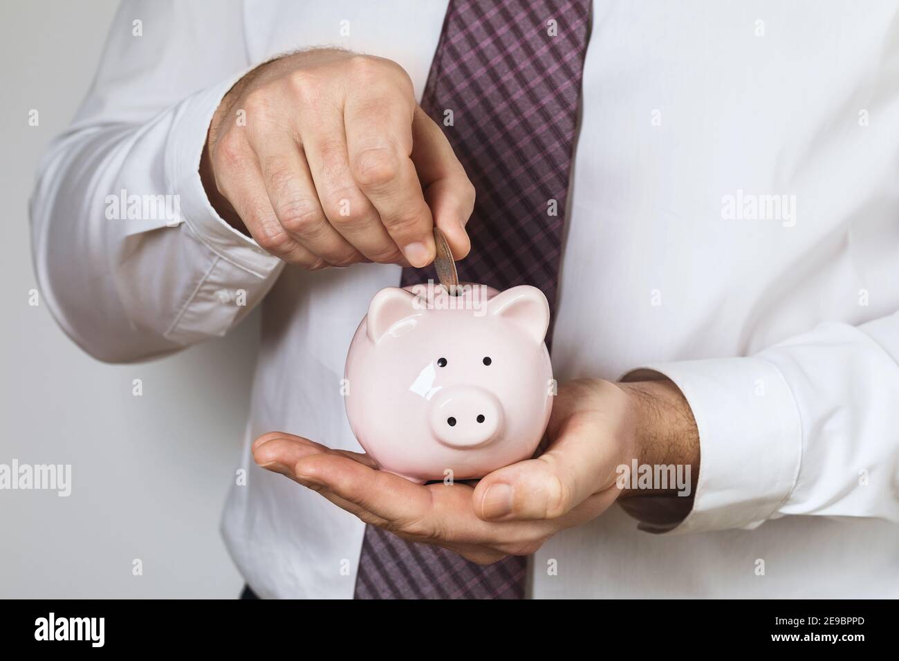Der Büroangestellte steckt eine Münze in das Sparschwein. Konzept zum Thema persönliche Entwicklung. Stockfoto