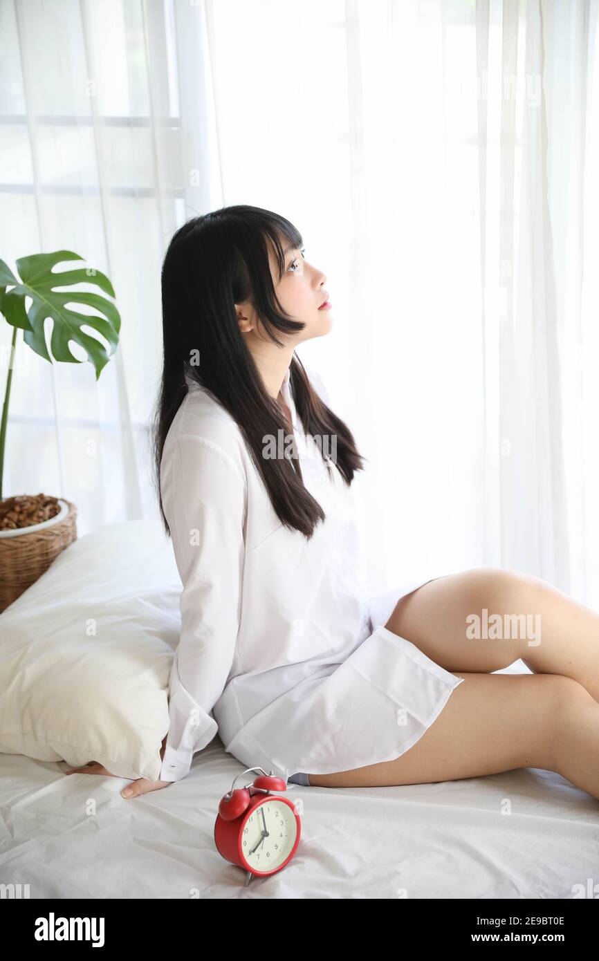 Portrait schöne asiatische Mädchen sitzen mit Uhr im weißen Schlafzimmer Stockfoto
